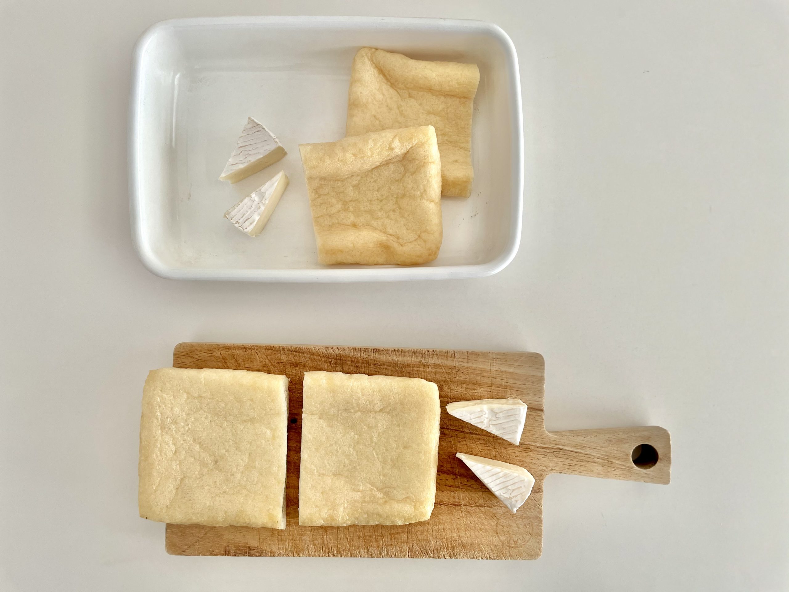 油揚げを横向きにまな板の上に置き、縦に半分に切る。<br />
カマンベールチーズも半分に切る。